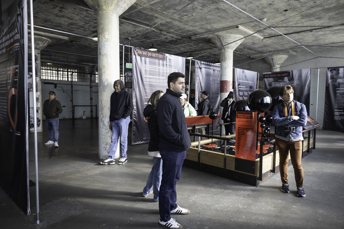 People stand in an exhibit looking at interpretive banners near a 3 dimensional installation with black spheres and a world map.