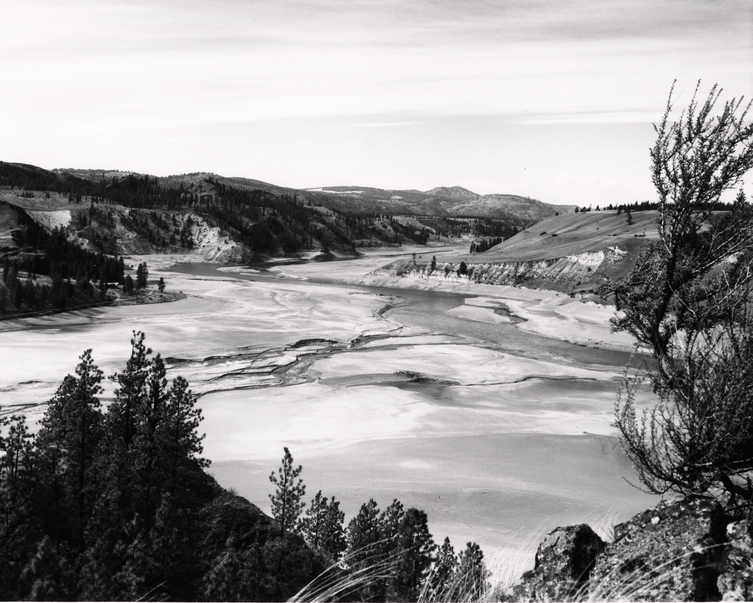A black and white photo of a river in a valley. 