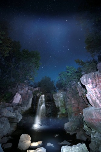 waterfall at night under stars with mist above and in front of the water.