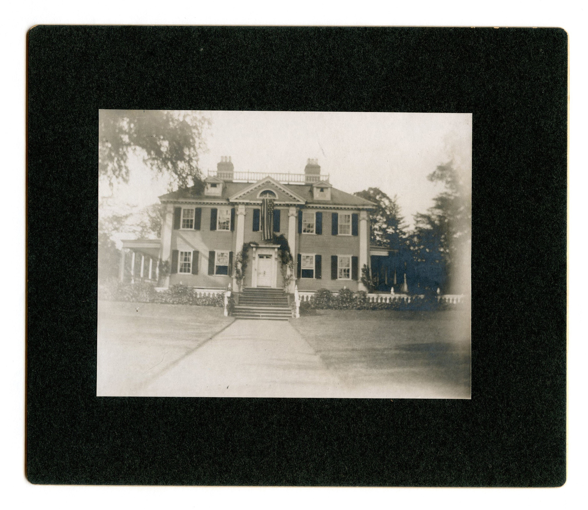 Facade of Georgian mansion with flag hanging out center window. Black and white photo.