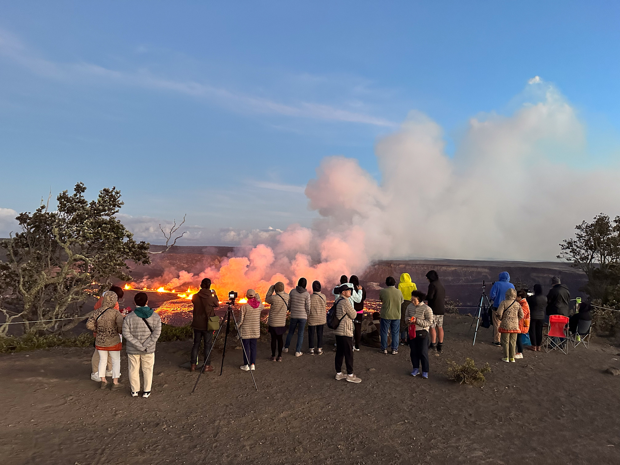 A group of visitors photographing and viewing the eruption from Kīlauea Overlook at sunrise. 
