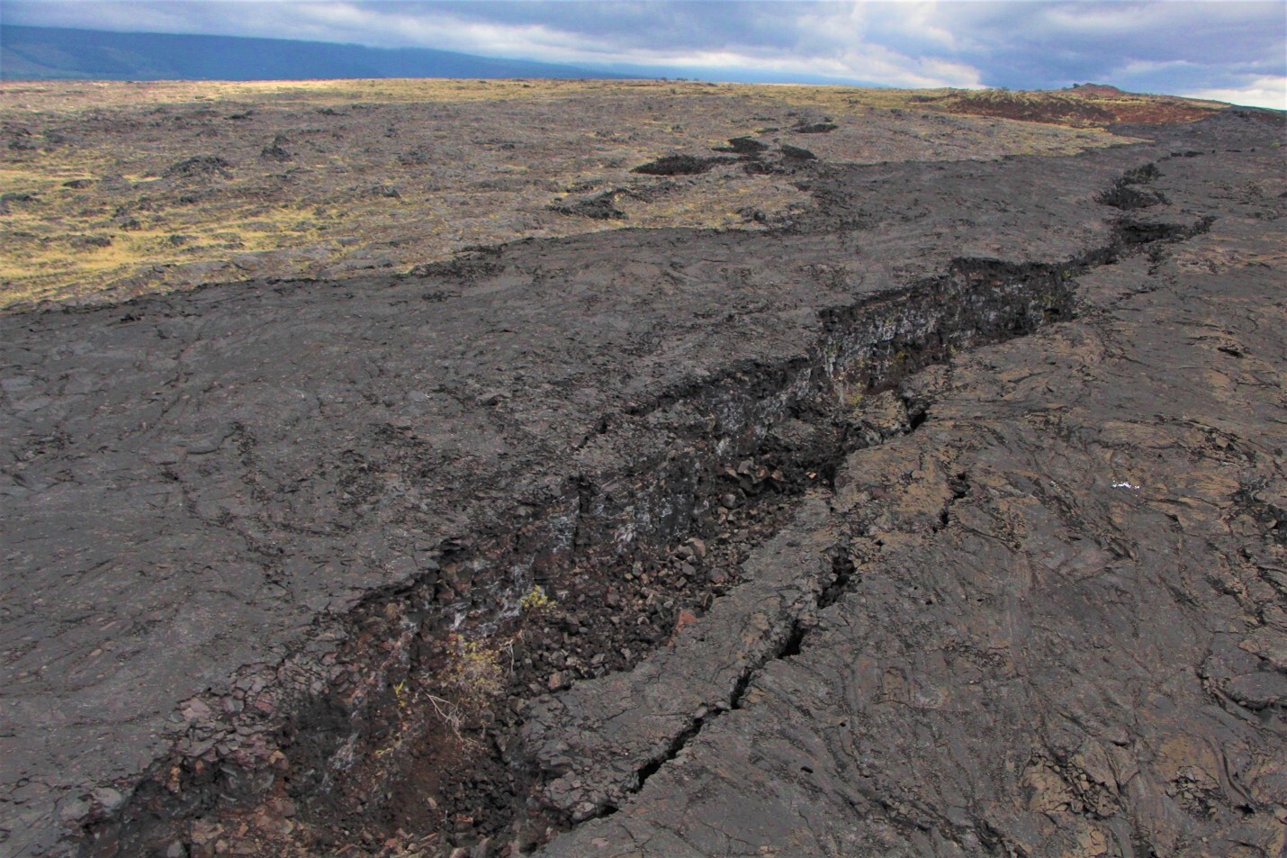 A large long earth crack dominates a dry and barren landscape 