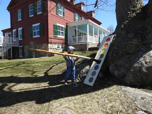 A child holds an oversize paintbrush next to a large easel