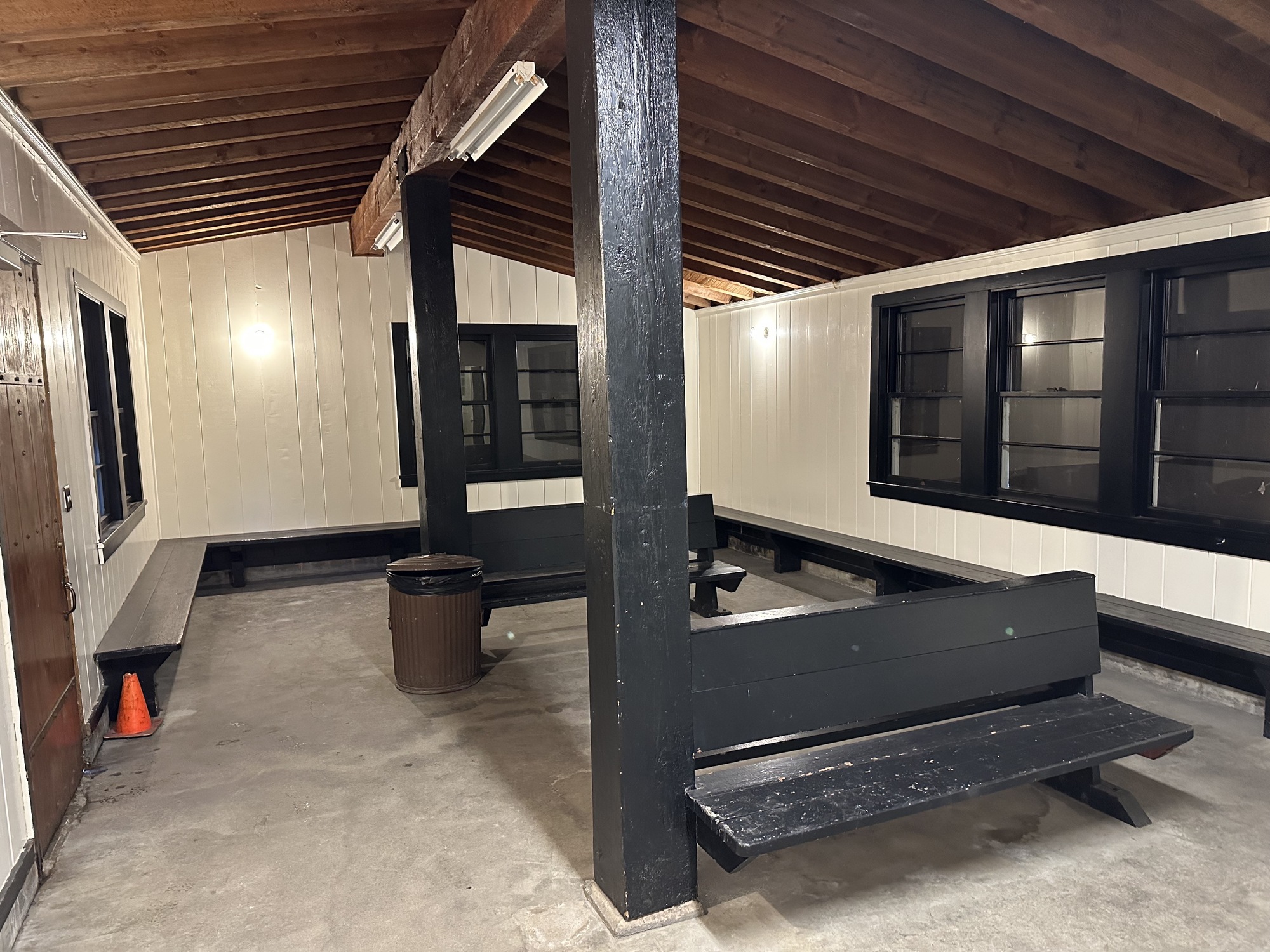 The interior of a small building with a common warming room. The walls are lined with benches with two benches in the middle. The floor is concrete with a wood beam roof. 
