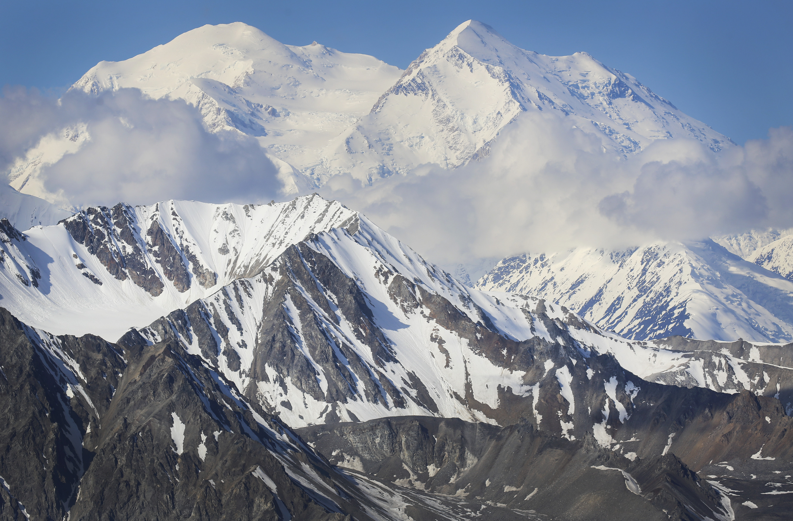 a huge snowy mountain, with clouds covering the middle-section of the peak