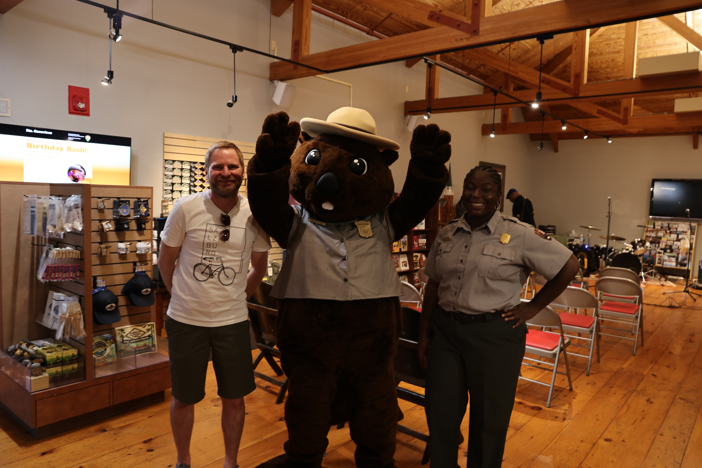A Park Ranger Beaver Mascot stands between a man in a t-shirt and shorts and a Park Ranger in uniform.