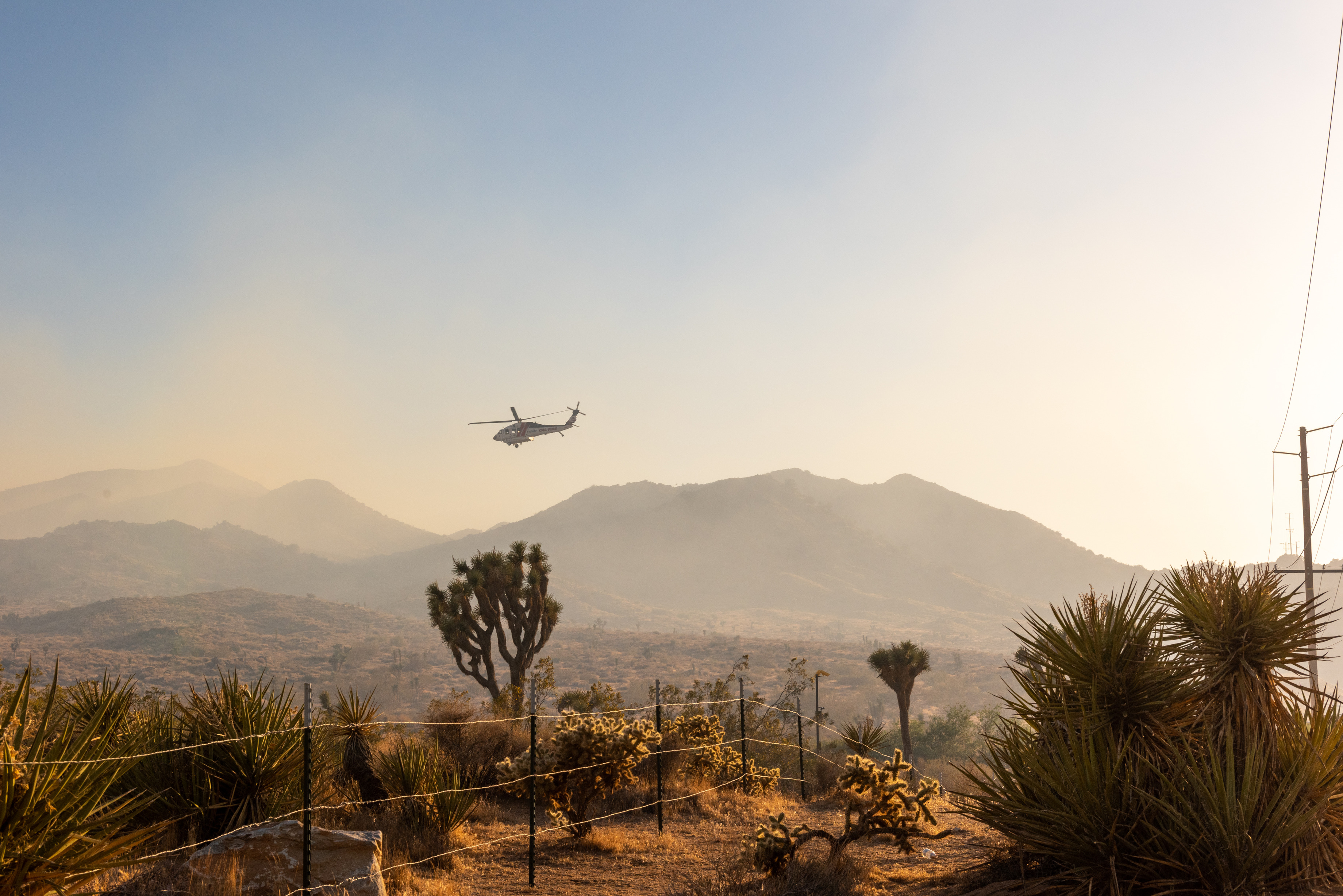 A helicopter flies above smoke and a desert landscape.
