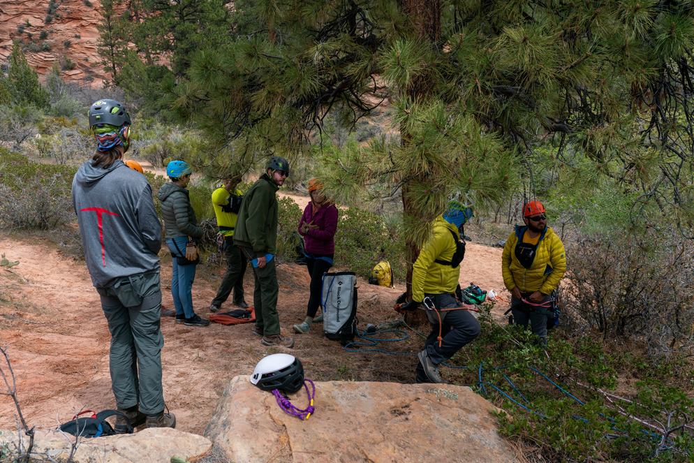 Eight search and rescue team members stand and discuss rescue training near a rope.