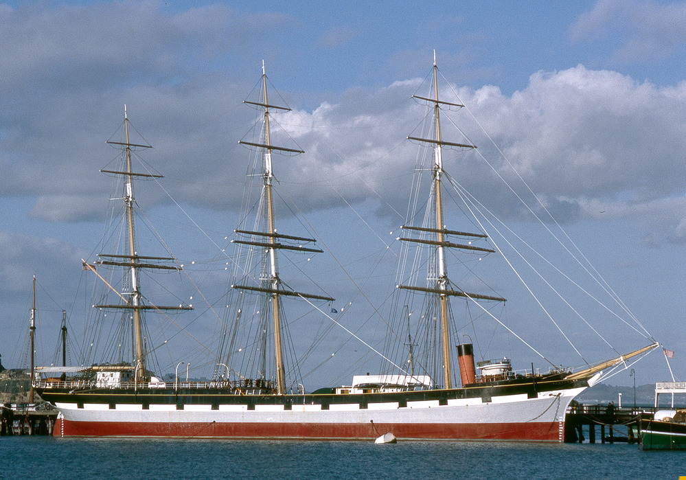 A three-masted, square-rigged sailing vessel moored along a pier in San Francisco.