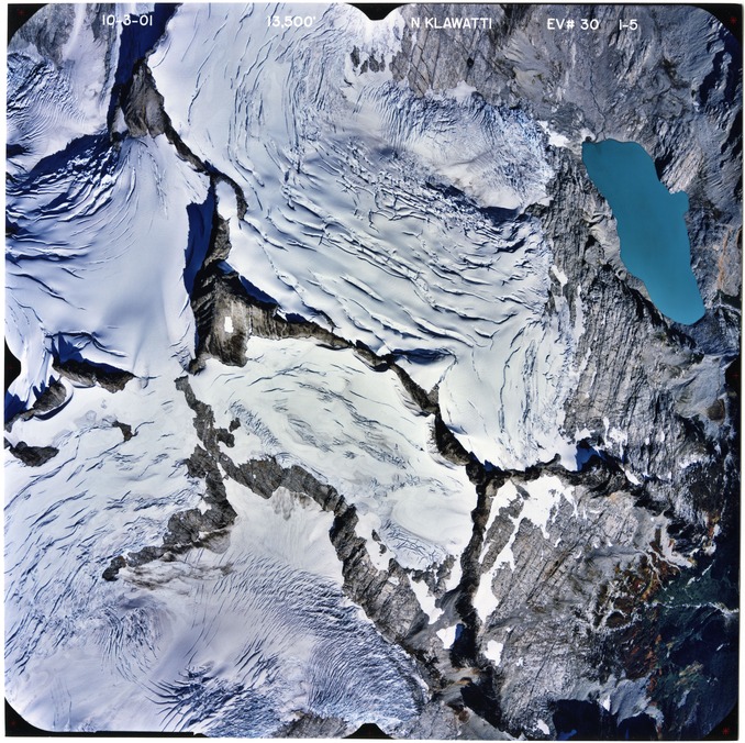 Color aerial photograph of glacier, snowfields, and alpine lake on mountain peak.
