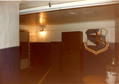 An underground room with a heavy door. A strategic Air Command logo is painted on one wall.