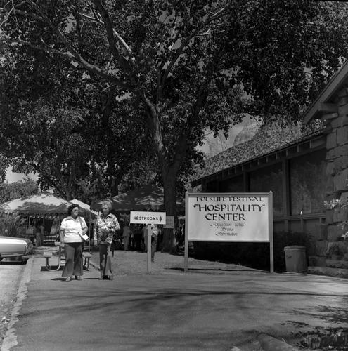 LaDessa Miller (left) and Leatta Olsen (right) walking near entrance sign for the second annual Folklife Festival, Zion National Park Nature Center, September 7-8, 1978.
