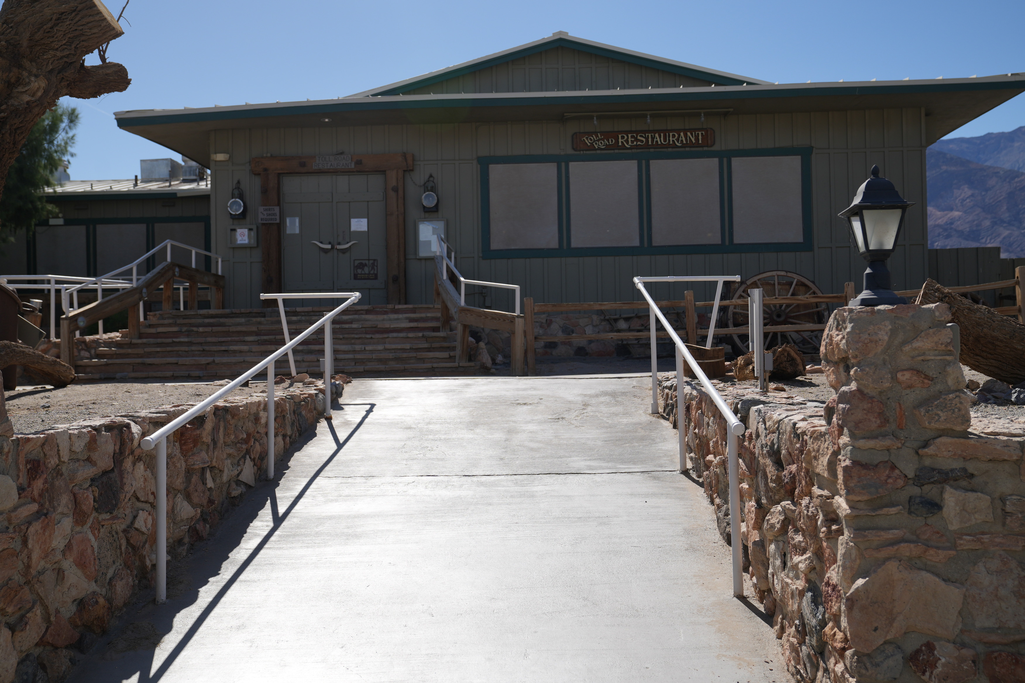 Stovepipe Wells restaurants' ramp entrance. A ramp with two railings that leads to a set of stairs and series of additional ramps. They lead to the alternative entrance to both of the restaurants. The grade is moderately steep and smooth concrete.