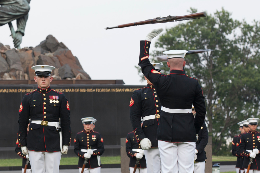 Marines in dress uniform toss rifles in front of the memorial