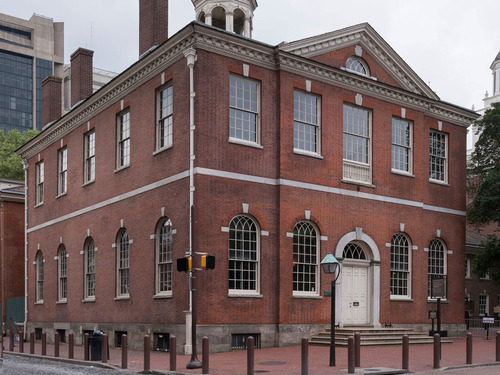 Color photo of the exterior of a two story red brick building, very symmetrical in appearance with a triangular pediment.