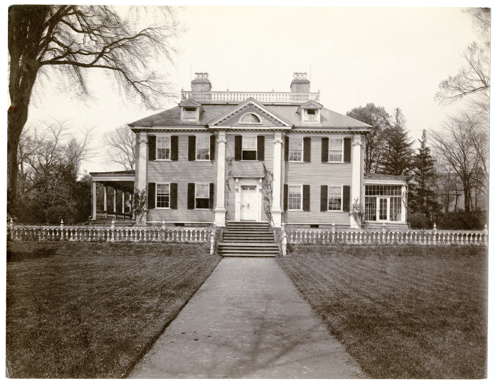 Facade of Georgian house with lawn in front, one of the flanking porches glassed in