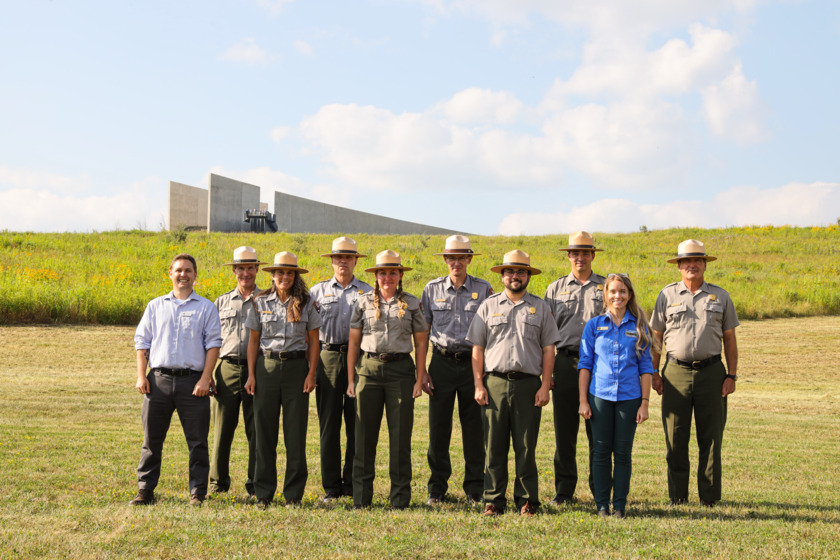 A group photo of Flight 93 park rangers, SCA, and Visual Information Intern 2021 at the Memorial Plaza. Visitor Center is shown from a distance.