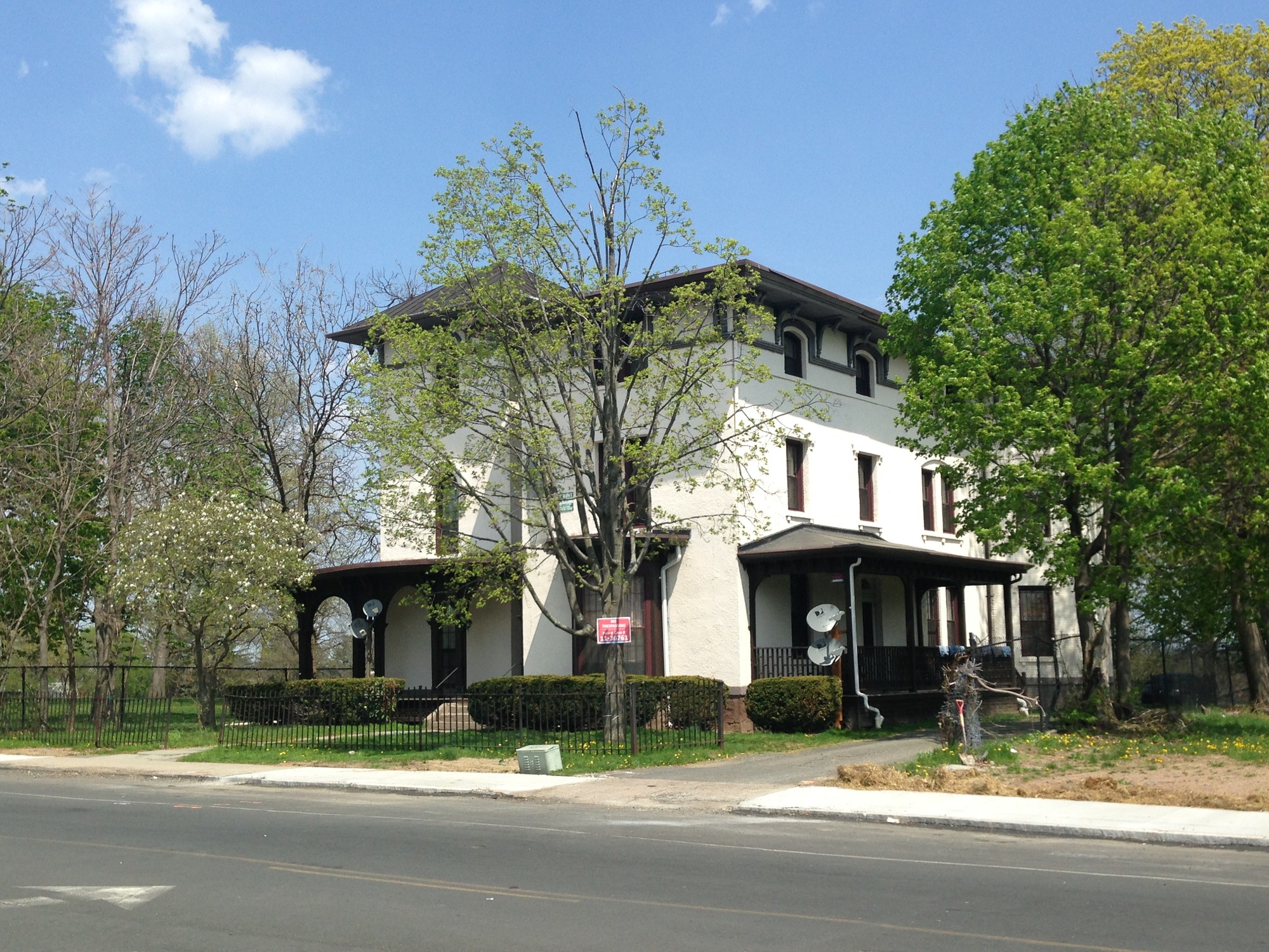 White house with dark porch and window trim. Iron fence along the sidewalk.