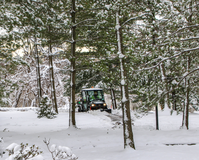 Small vehicle plowing snow on a trail under tall trees