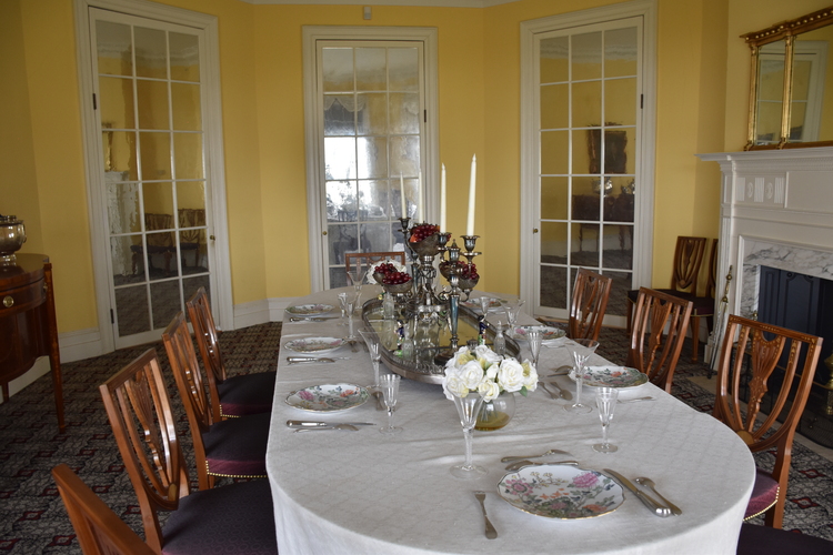 A table draped in white cloth and surrounded by chairs, set with china and silver ware. 