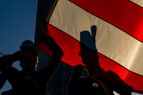 The shadows of two people wearing historic soldier outfits holding the American flag.