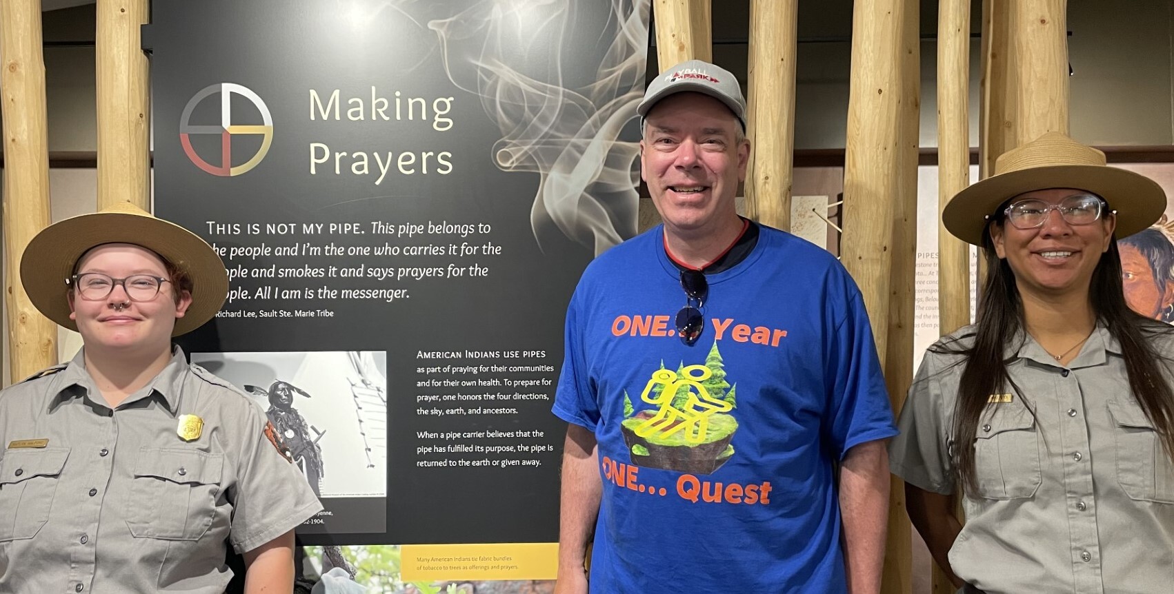 3 people standing in front of an exhibit panel indoors. 