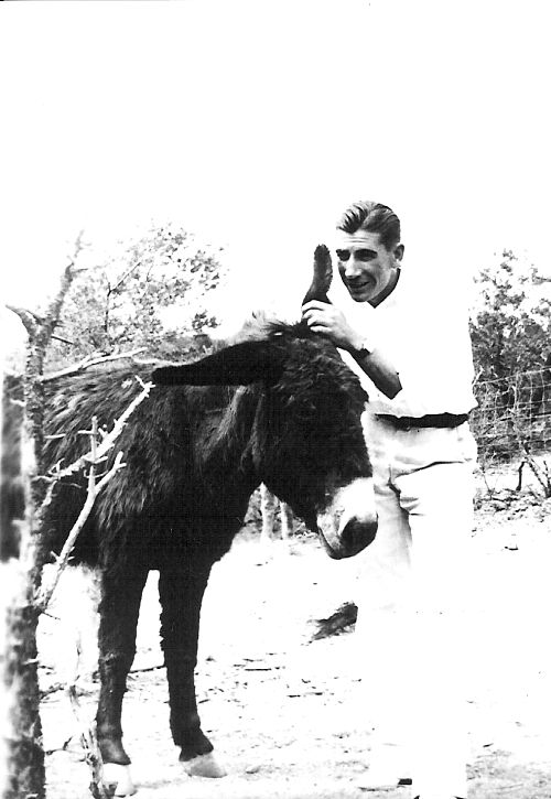 Black and white photo of man whispering into a mule's ear. 