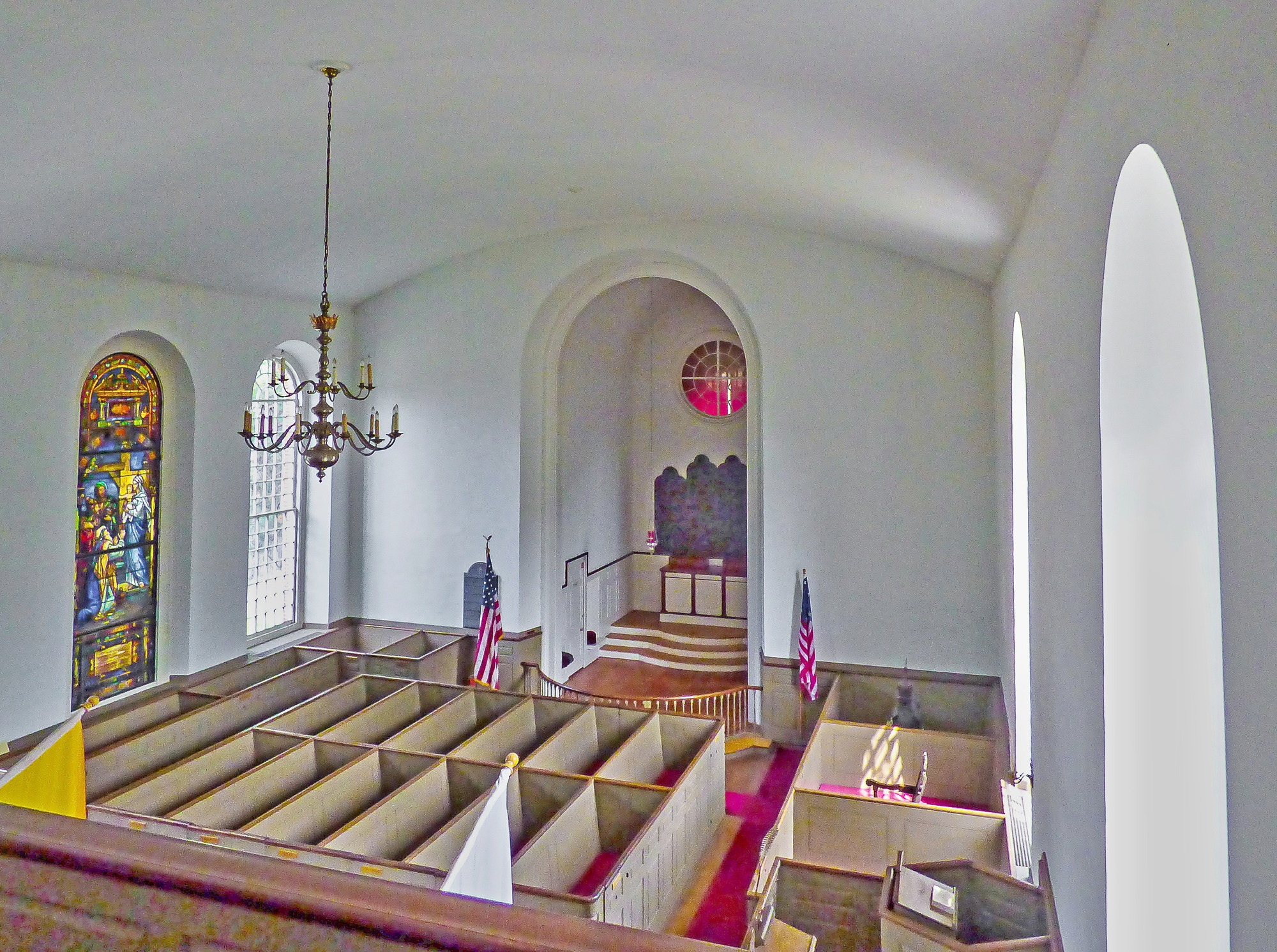 color photo of the interior of a historic church, with box pews, flags, a chandelier and stained glass window visible.  