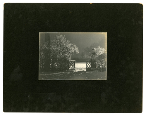 Black and white photograph of snow covered front gate, mounted on black paper.