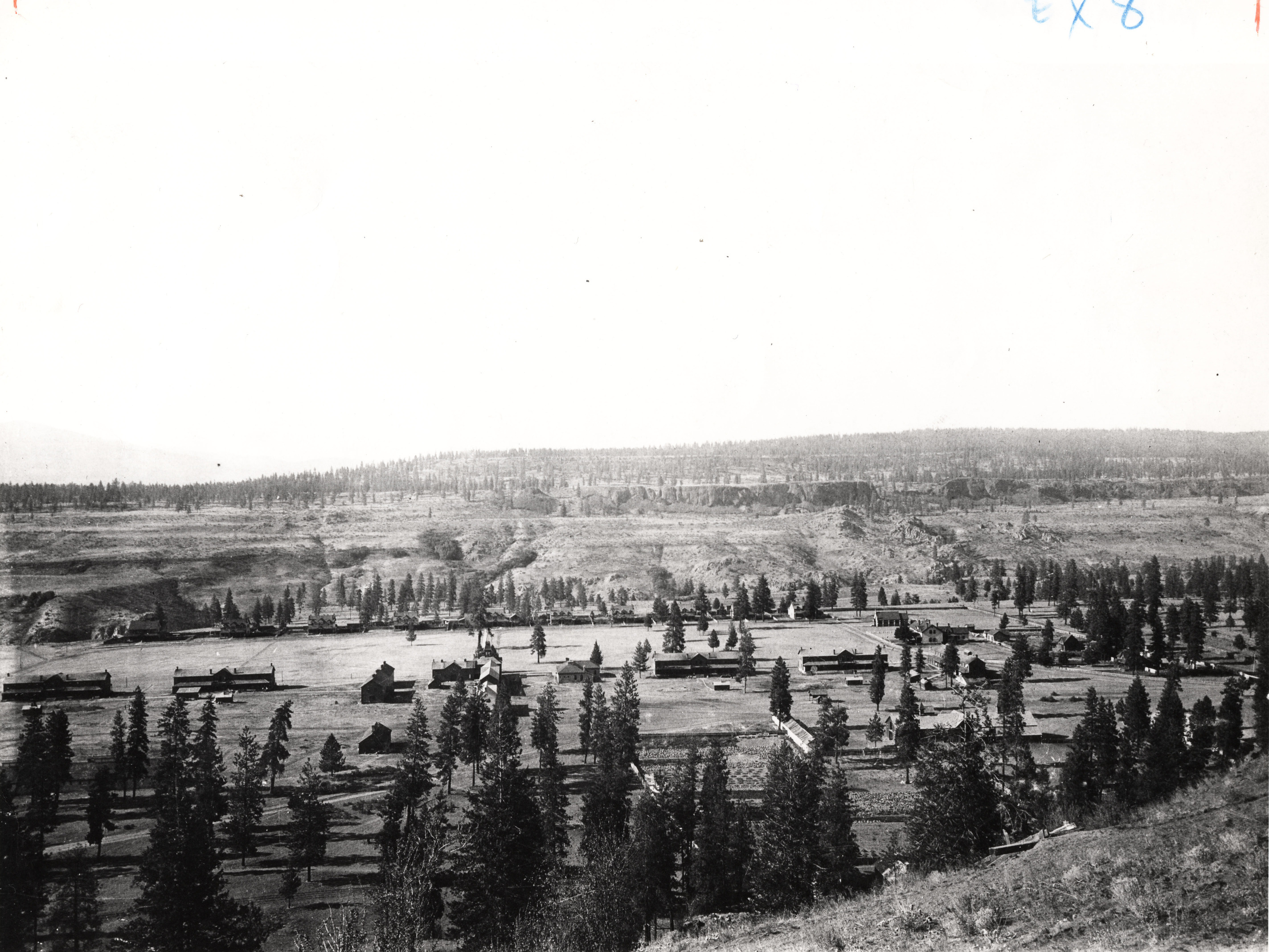 Black and white photograph of several long buildings in a wide forested valley