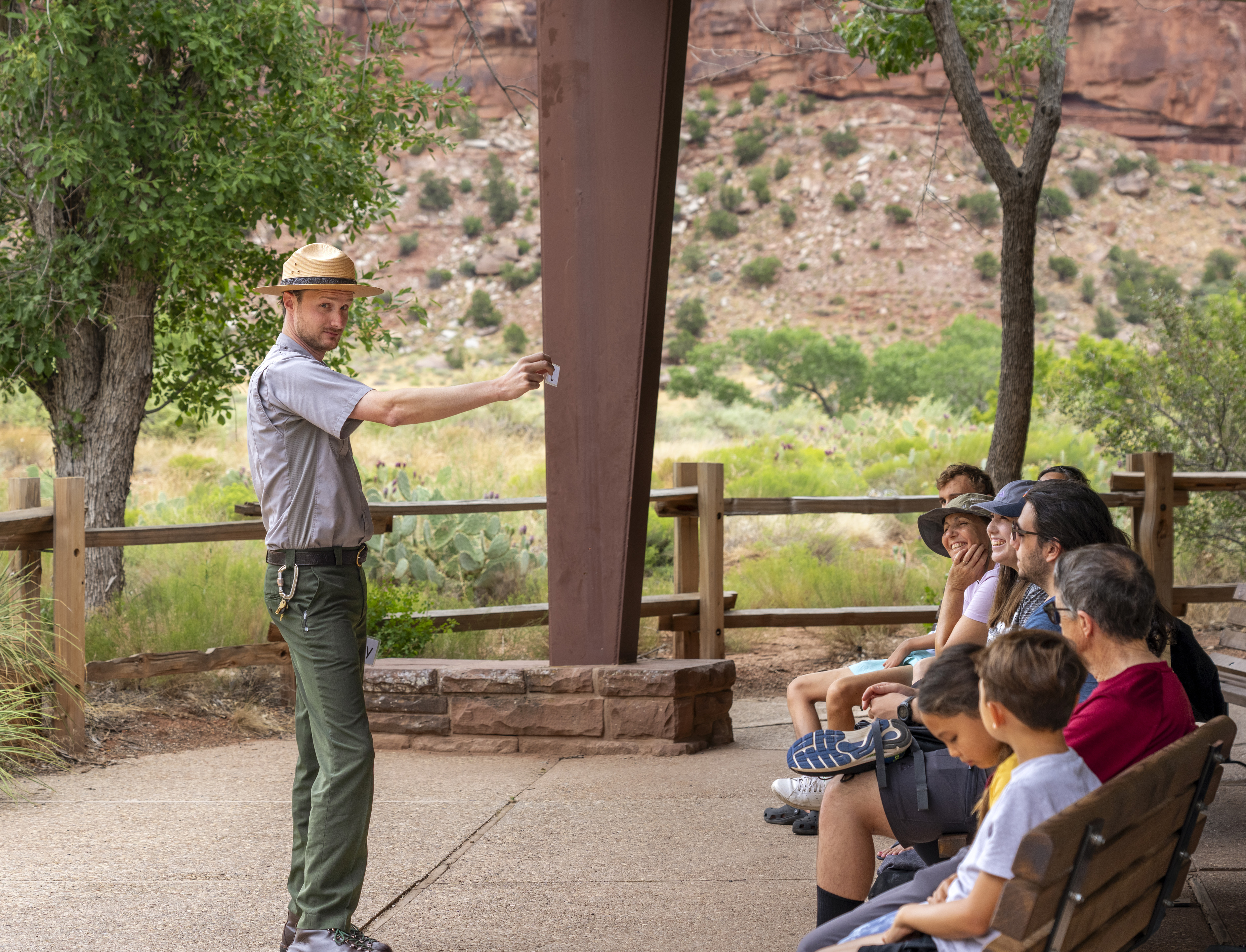 A ranger in a flat-hat holds up a card to seated visitors,. 