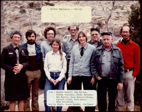 A group of women and men employees at Arches National Park, with some wearing the park ranger uniform.  Text reads: Arches Employees 1982-83, L-R-Maxine Newell, Jim Stiles, Sherma Bierhaus, Nibby Mathews, Ben Hardin, Joan Swanson-Young, Carroll Clark, Dave Baker, Mike Salamacha. Not in Photo: Steve Swanke, Jim Capps