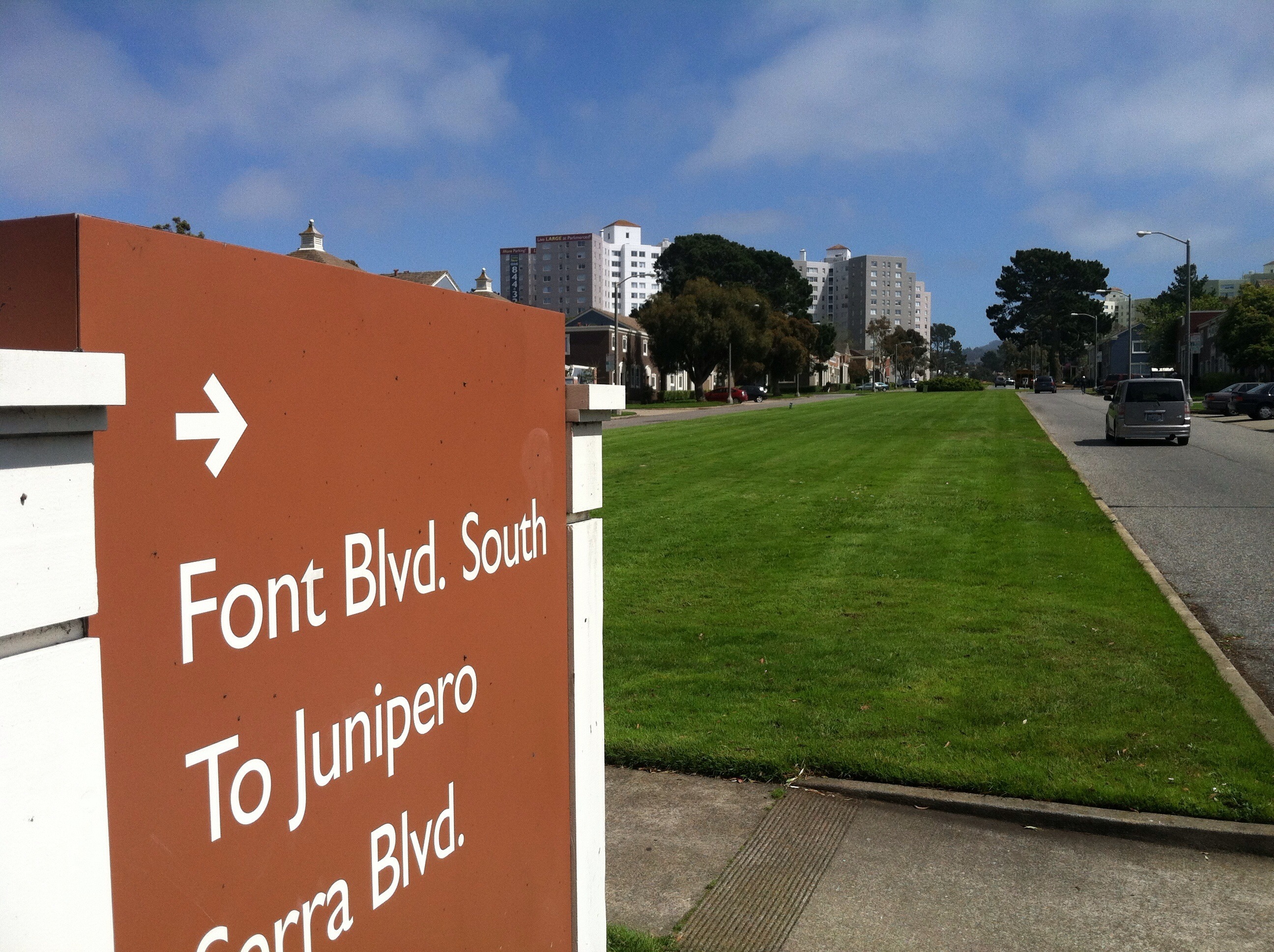 A sign in front of a green lawn says Font Blvd. South to Junipero Serra Blvd.