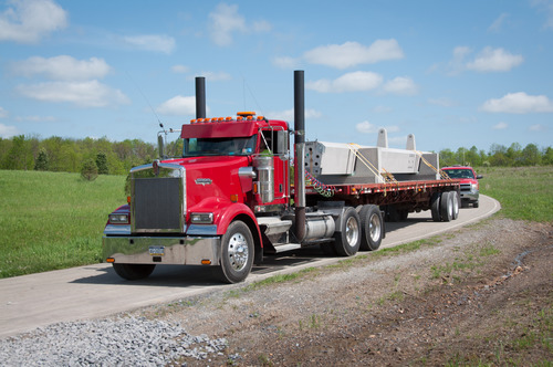 Long concrete structure on the back of a truck driving on a road. 