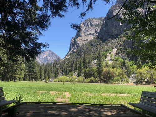 A wood deck overlooking a green meadow with tall granite cliffs in the background.
