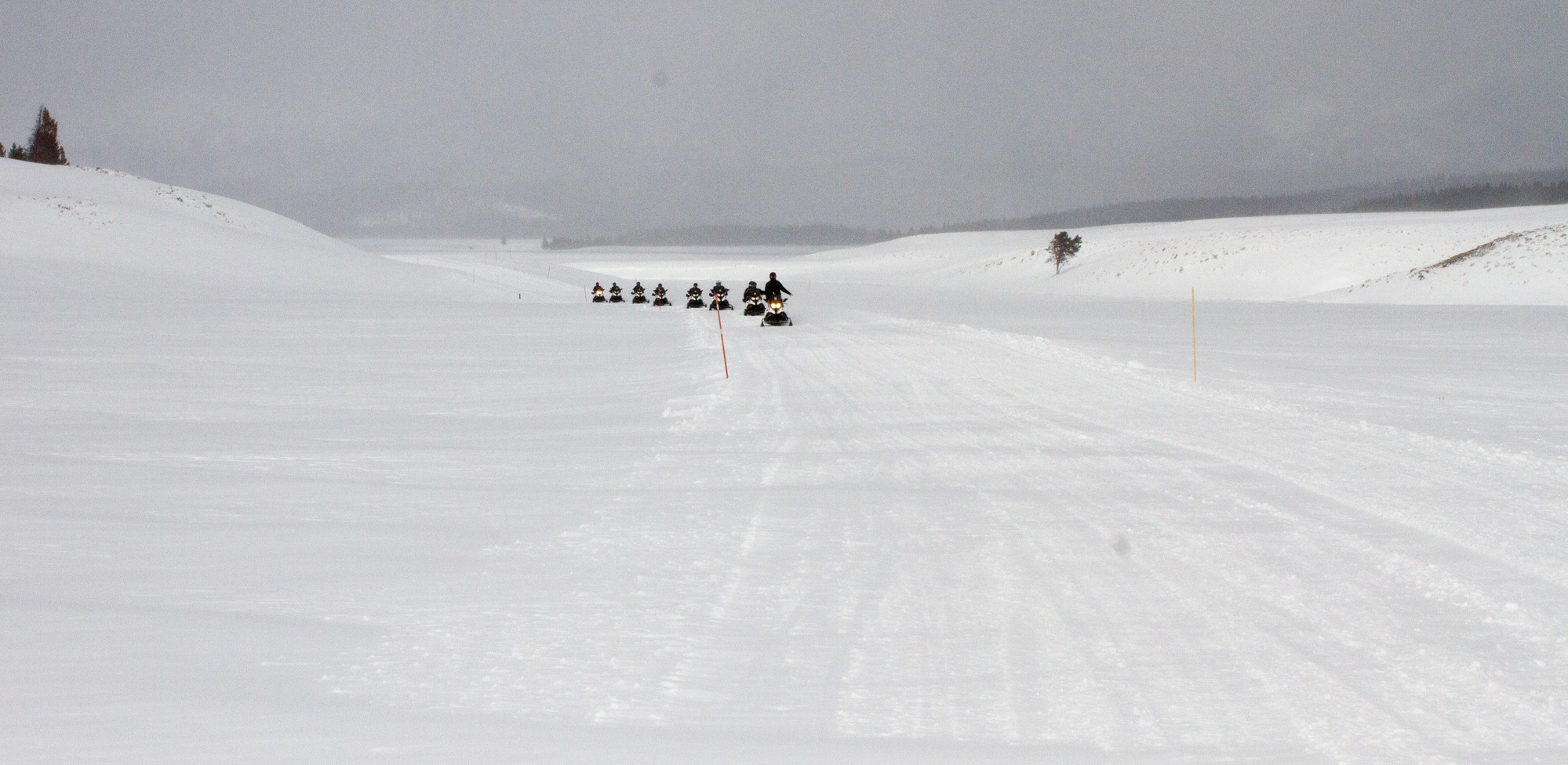 Snowmobilers on a packed road in an open snow covered valley