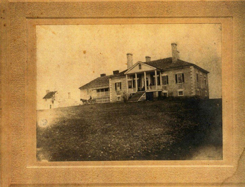 A framed and matted, yellowed 1800s photo shows the front of a porticoed plantation house.