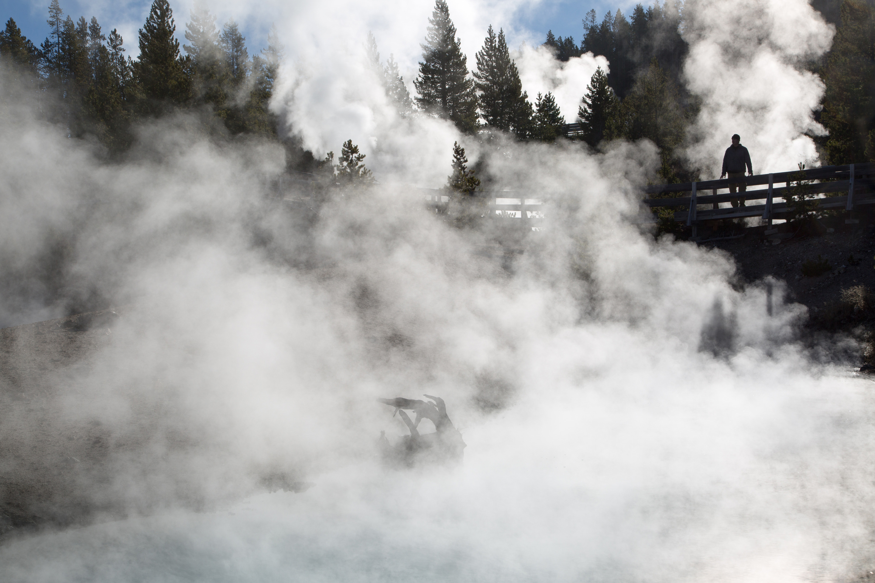 A silhouette of a person standing on a boardwalk looking this way into a steamy pool.