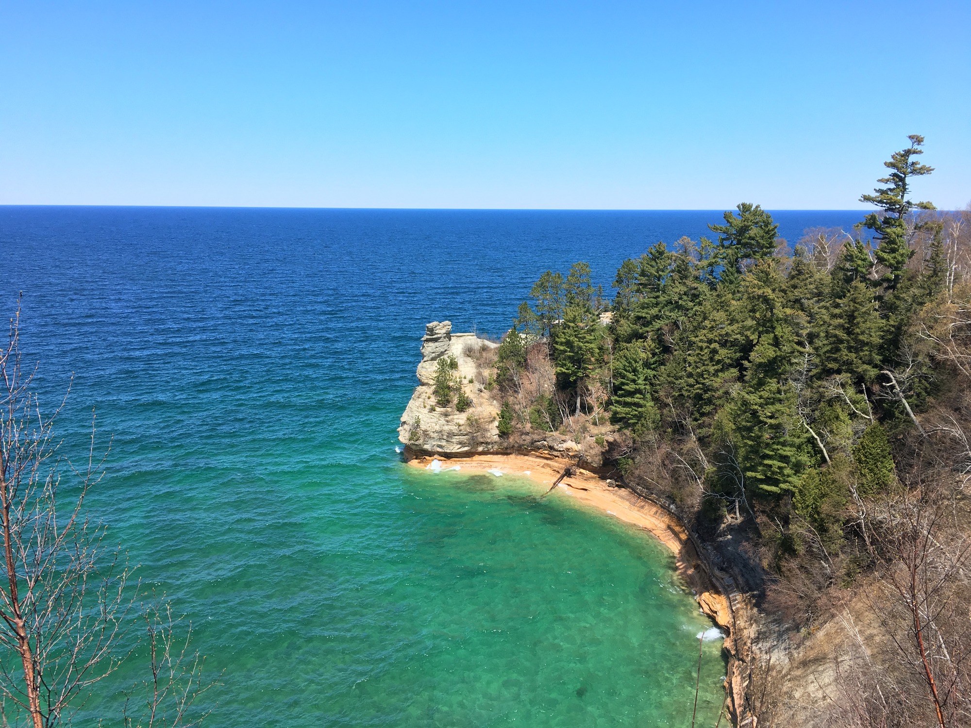 Sandstone rock formation that looks a little like part of a castle with a turret on top. It is at the end of a tree covered cliff that sticks out into Lake Superior.