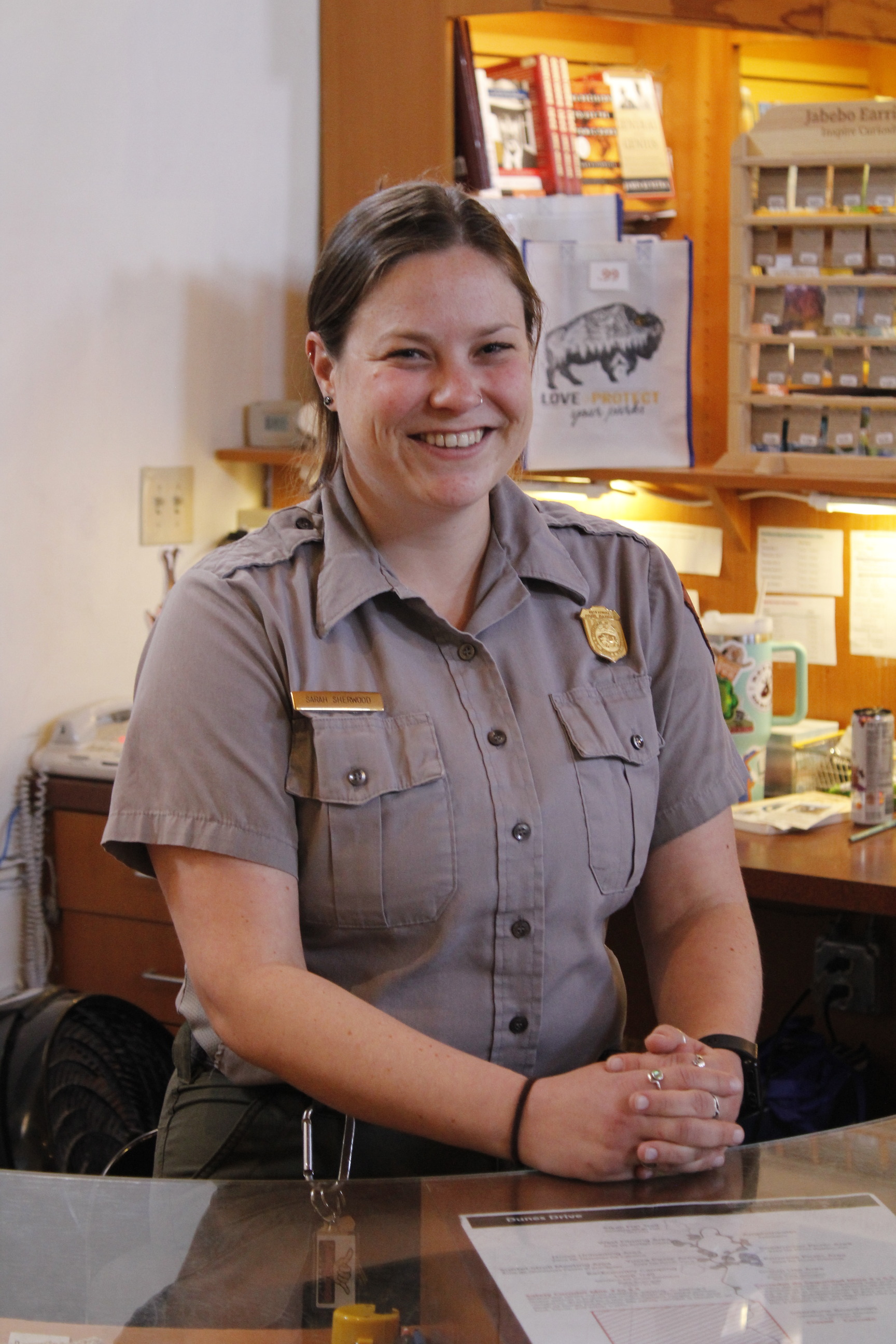 A woman wearing the National Park Service uniform sits at a desk to pose for a photo. 
