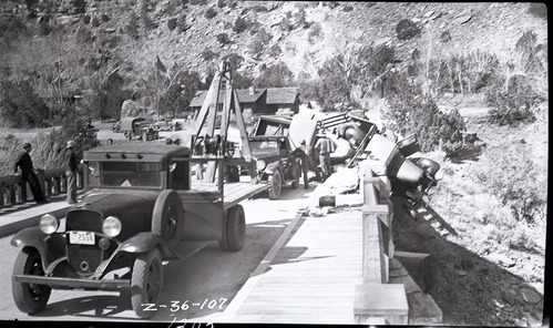 Vehicle accident on the Virgin River bridge of the Zion-Mt. Carmel Highway. View of overturned truck being removed from the bridge abutment and righted by tow truck workers, and other equipment.