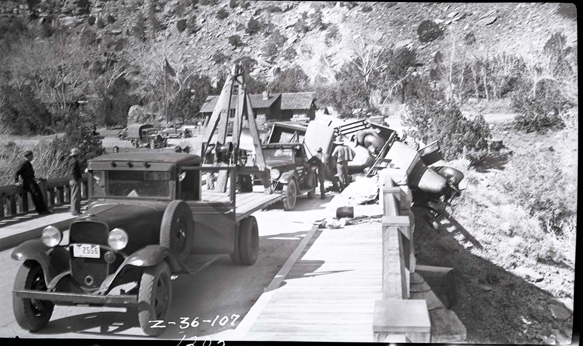 Vehicle accident on the Virgin River bridge of the Zion-Mt. Carmel Highway. View of overturned truck being removed from the bridge abutment and righted by tow truck workers, and other equipment.