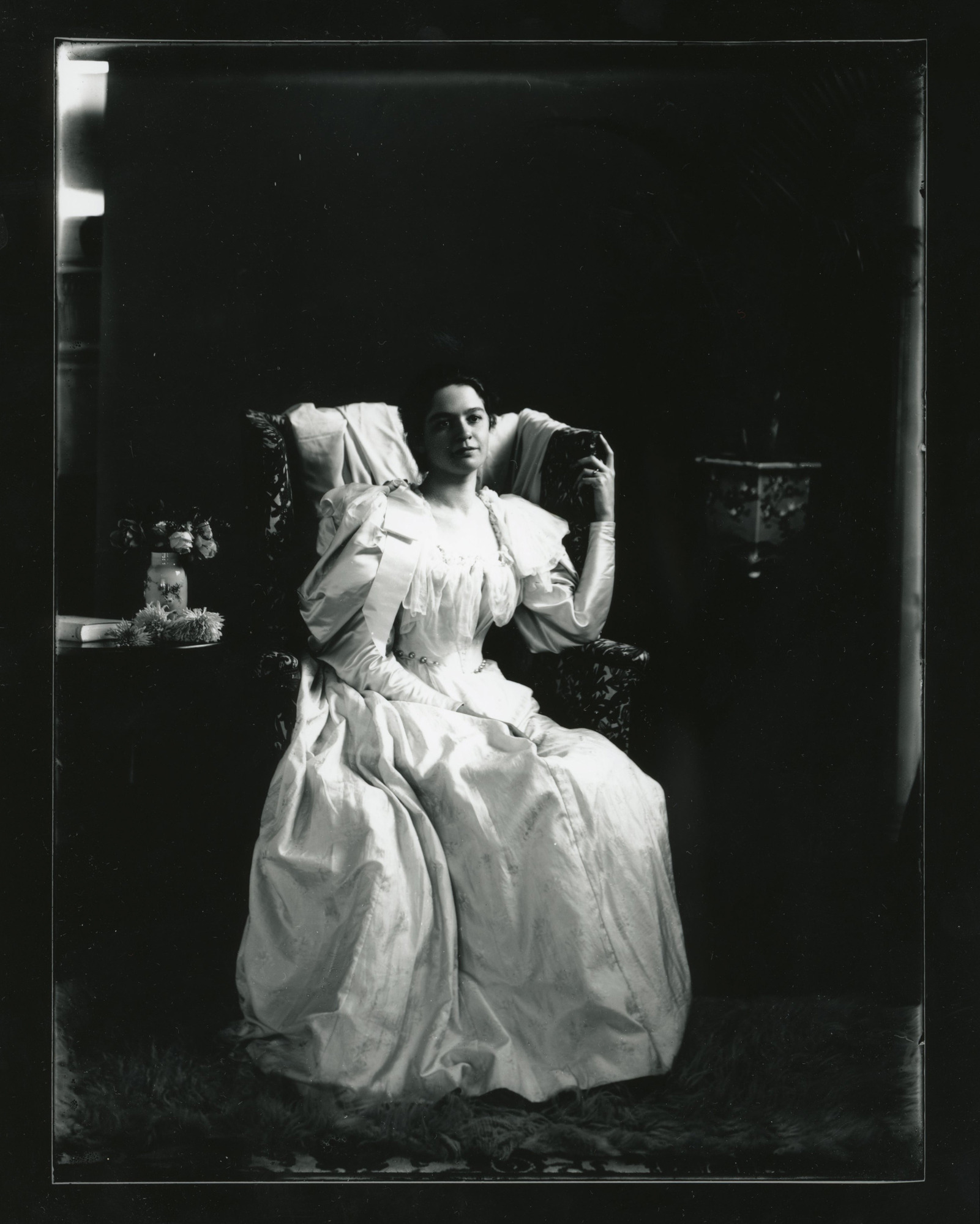A young white woman dressed in a puffed-sleeve dress sits in an upholstered chair.