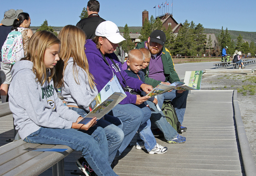 Parents and four children sitting on bench outside of Old Faithful Visitor Center studying books