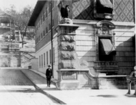 A man poses beside a stone pillar with an eagle on top, near the corner of a large bathhouse building.