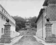 A road, framed by two eagle-topped columns, leads to a hillside with a bandstand on top.