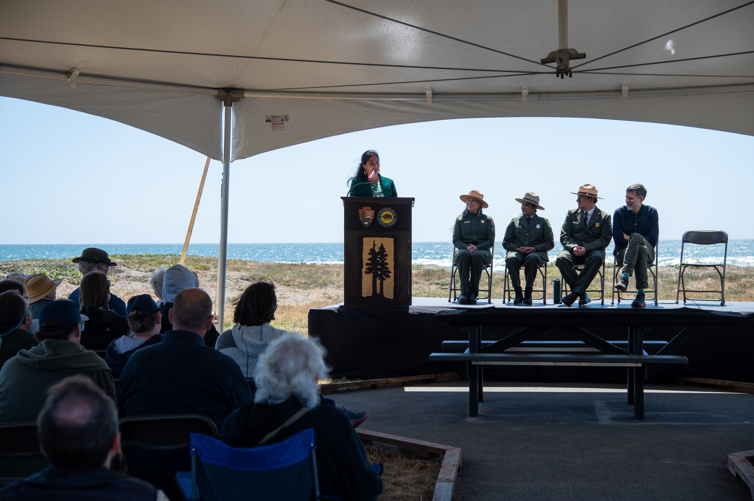 Ada Limón speaking at a podium. There are 3 other government officials seated on the stage to the right of her. 