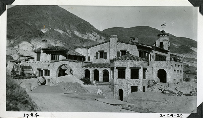 This is an historic black and white photograph from the Scotty's Castle Historic Photograph Collection, Death Valley National Park of Scotty's Castle Main House and Annex, exterior construction nearly complete. February 24, 1929. Photographed by Mat Roy Thompson.