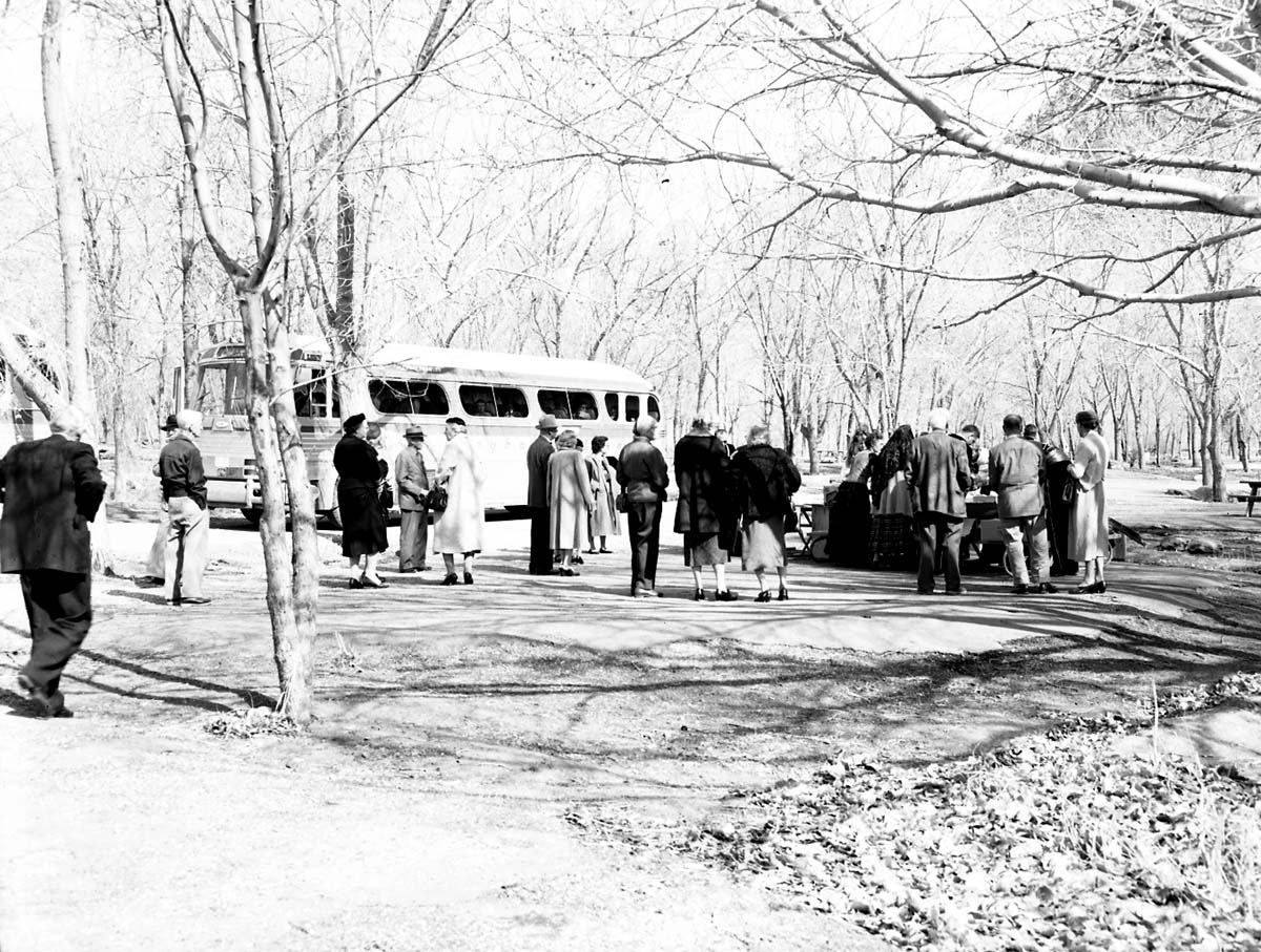 Visitors on Greyhound bus tour standing by picnic table. [Several men and women in traditional Spanish costumes?]