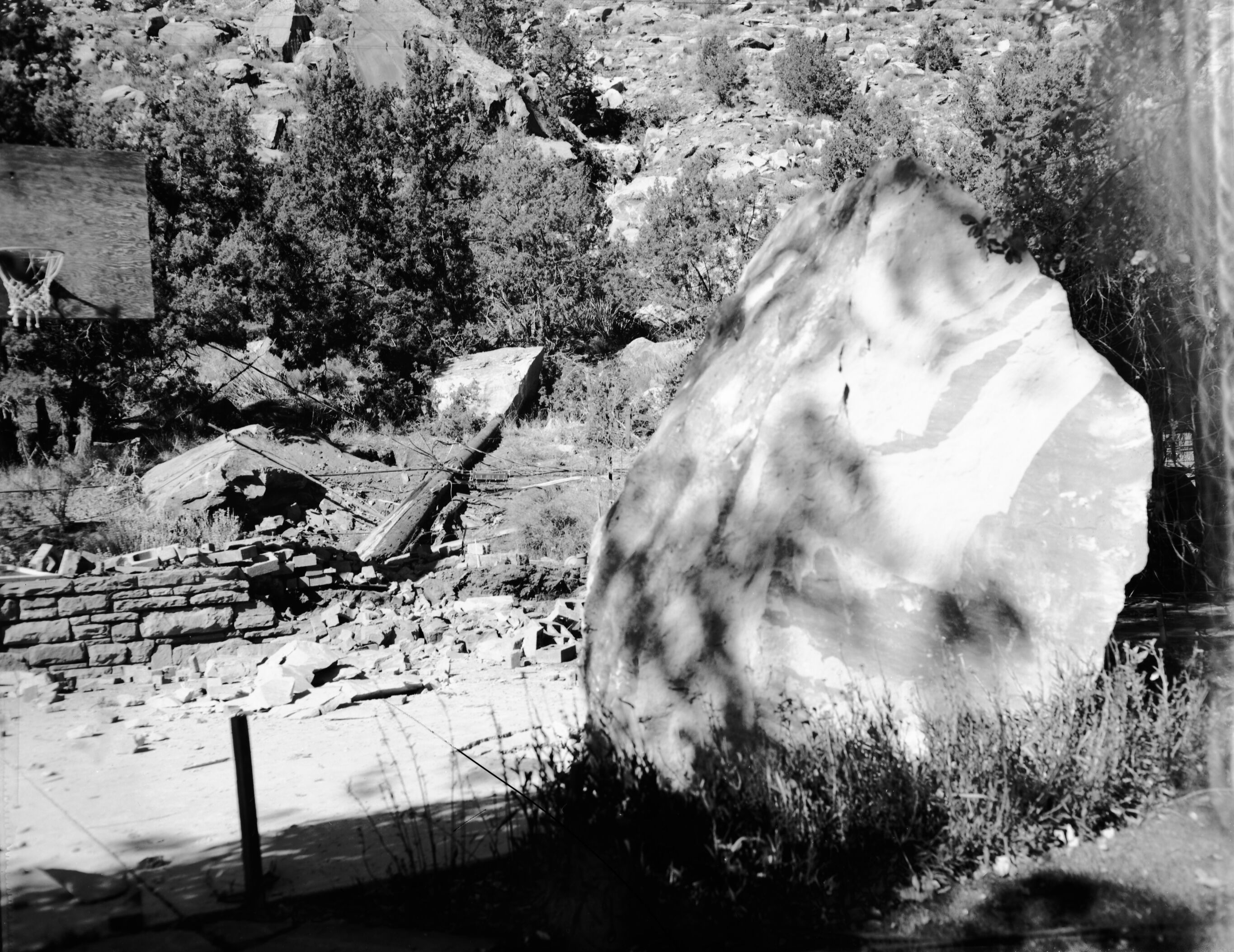 Rock fall behind Chief Ranger Fred Brueck's residence. Image shows large rock, ranger, house and woman sitting by rock fall depression.